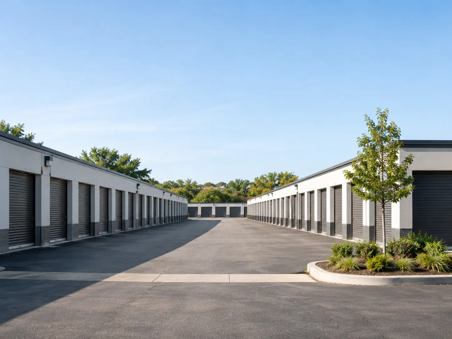Drive-up self-storage buildings with roll-up doors along a paved lane.